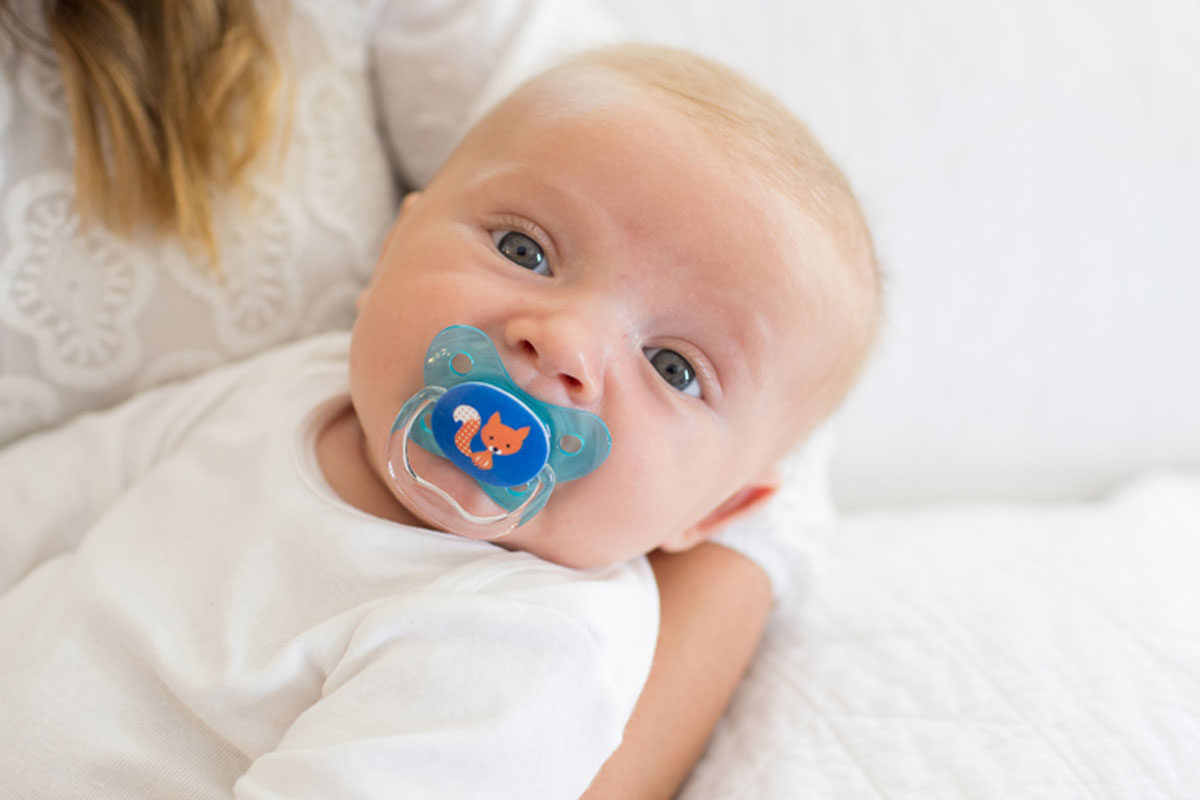 Baby in mother's arms with blue pacifier in mouth