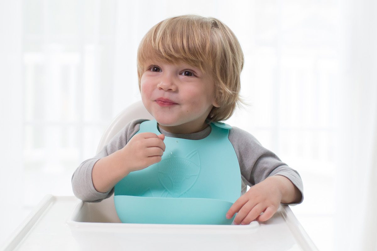 Toddler eating at high chair with Dr. Brown's silicone bib waiting for cauliflower pizza