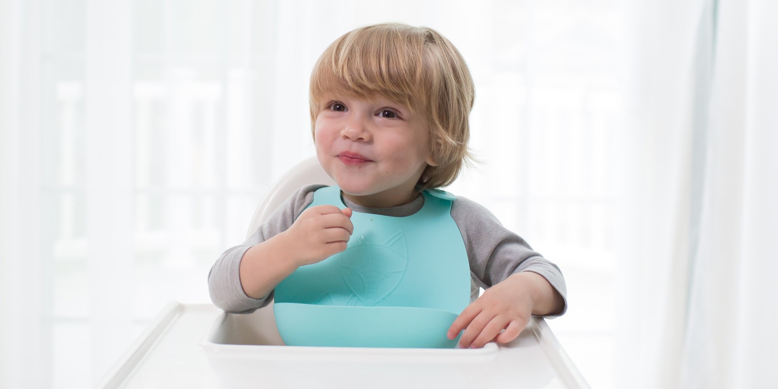 Toddler eating at high chair with Dr. Brown's silicone bib waiting for cauliflower pizza
