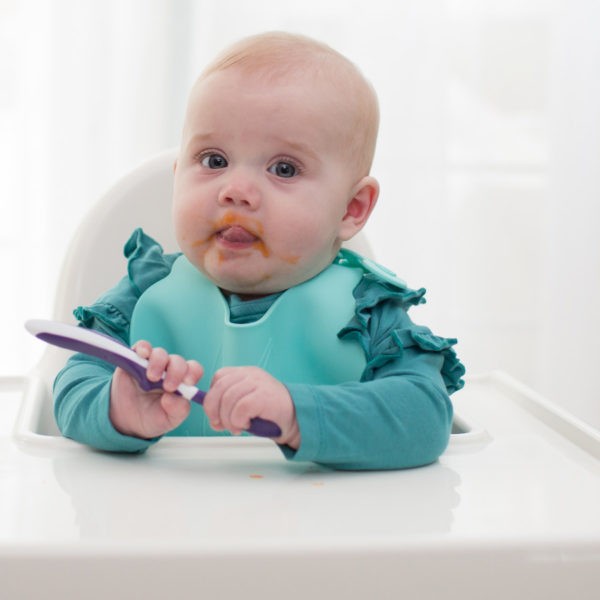 Baby with messy face holding spoon while sitting in high chair