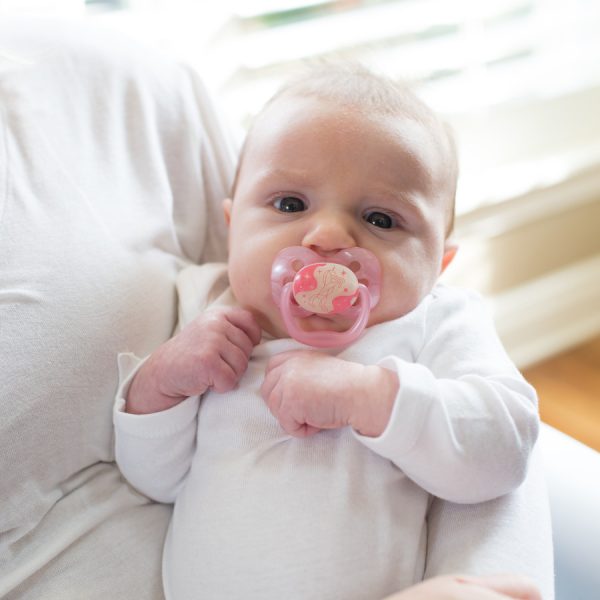 Baby in mother's arms with pacifier in mouth