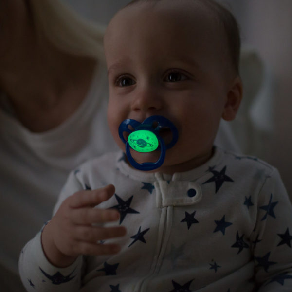 Baby in mother's arms in dark room with glow-in-the-dark pacifier in mouth