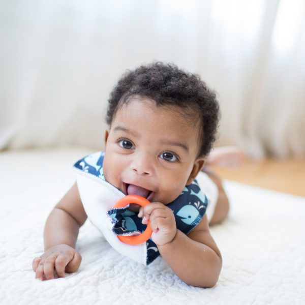 Baby laying on rug wearing bandana bib with teether in mouth