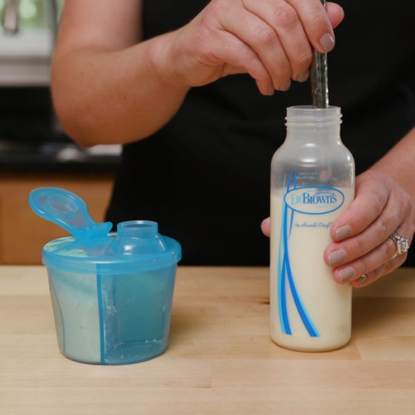 Woman mixing formula into bottle on counter next to formula dispenser