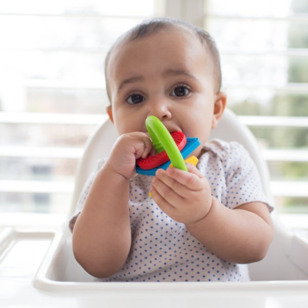 Baby in highchair with learning loop teether in mouth