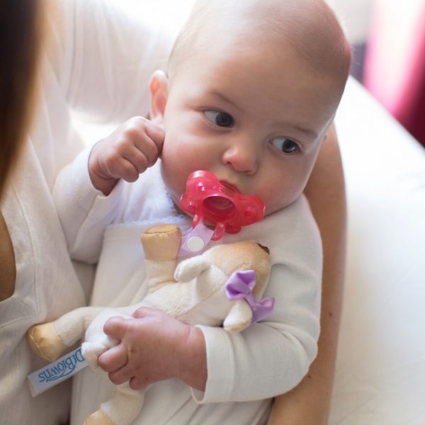Baby in mother's arms with deer lovey pacifier and teether holder in her mouth
