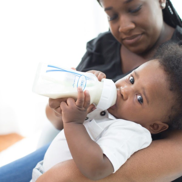A mom holding a baby who is drinking from a Dr. Brown’s Natural Flow® Options+™ Anti-Colic Wide-Neck Bottle