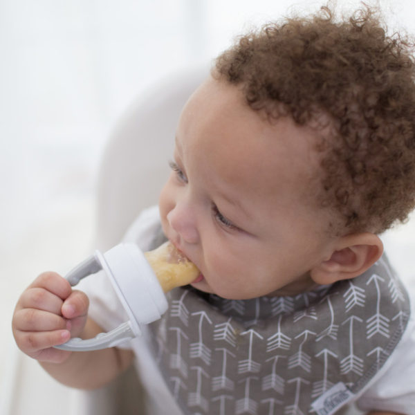 Baby sitting in highchair eating from silicone feeder