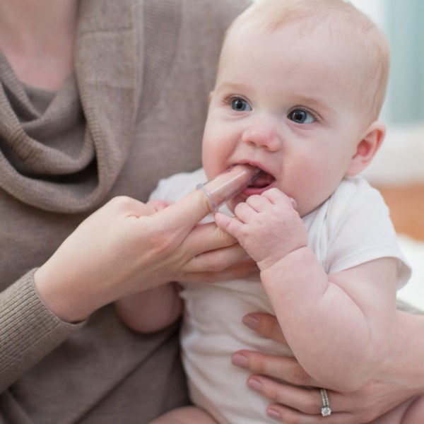 Image of mom holding baby in lap with finger toothbrush in baby's mouth