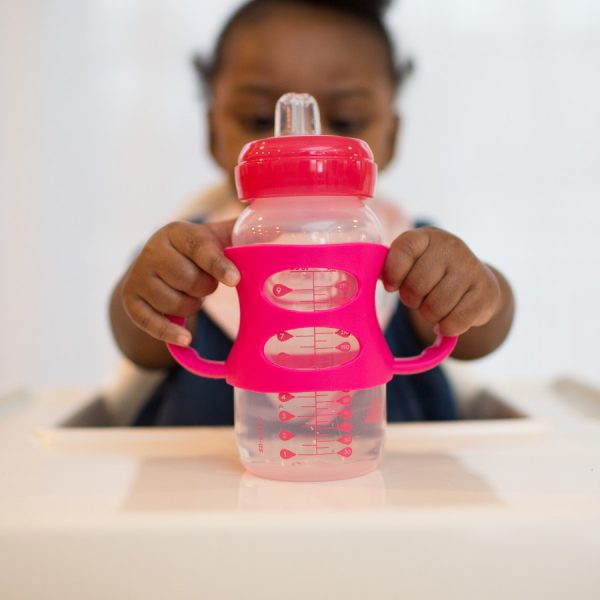 Baby sitting in highchair holding bottle with pink silicone handles