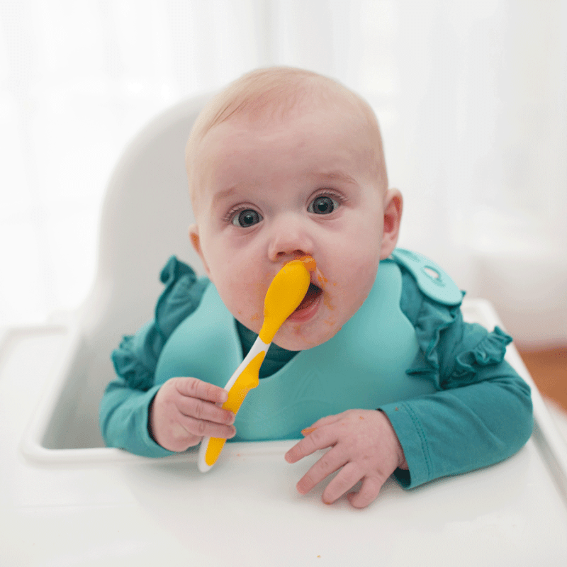 baby in highchair using feeding spoon