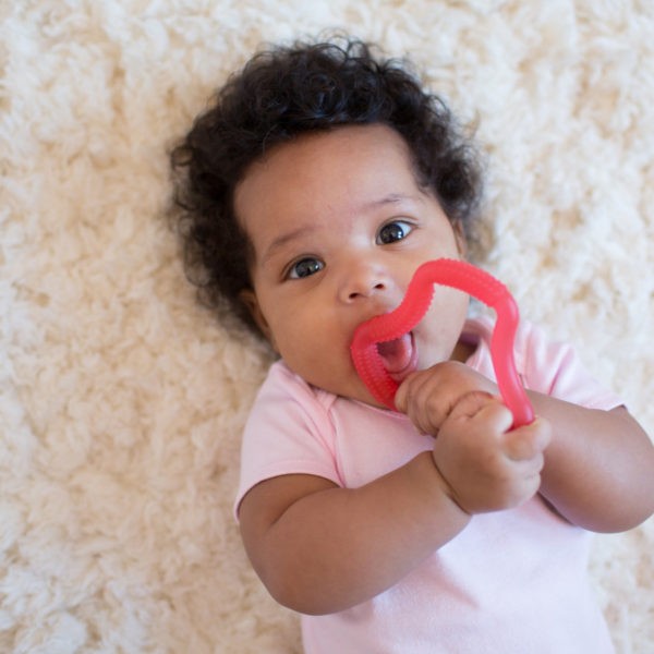 baby on rug with pink teether in mouth