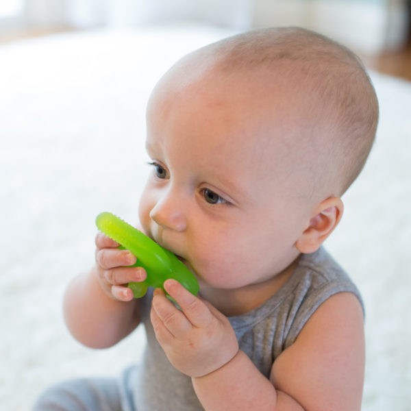 Baby sitting on rug chewing on green teether