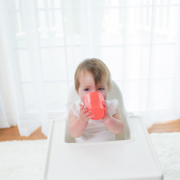 Baby in highchair drinking from red tumbler cup