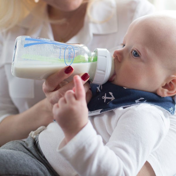 Mother holding baby who is drinking from a Dr. Brown’s Natural Flow® Options+™ Glass Wide-Neck Bottle 9 ounce