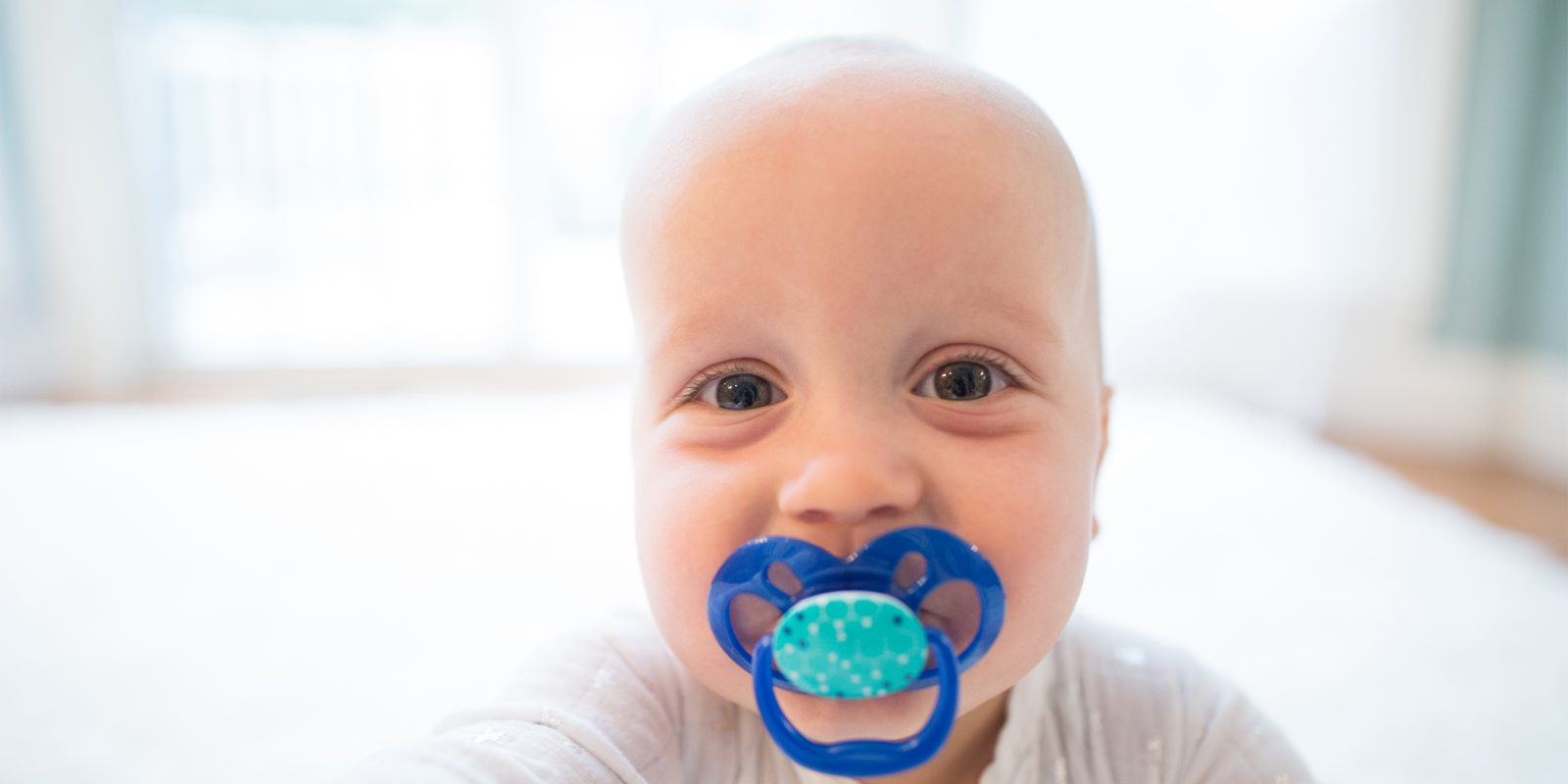 Up close image of smiling baby with pacifier in mouth