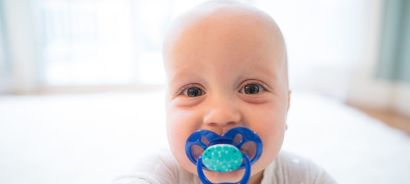Up close image of smiling baby with pacifier in mouth