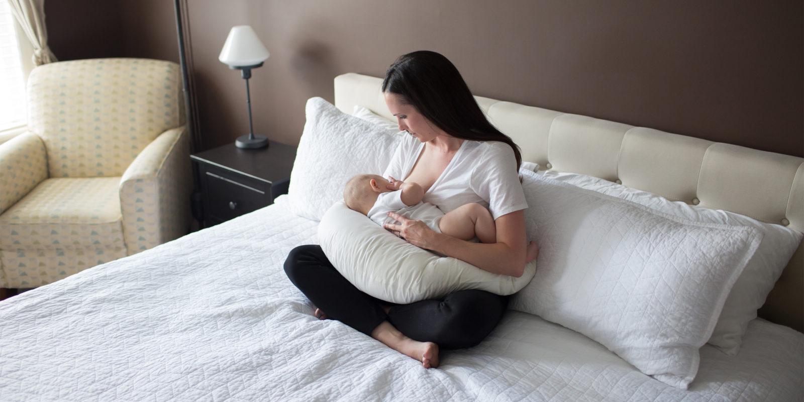 Woman sitting on bed breastfeeding baby