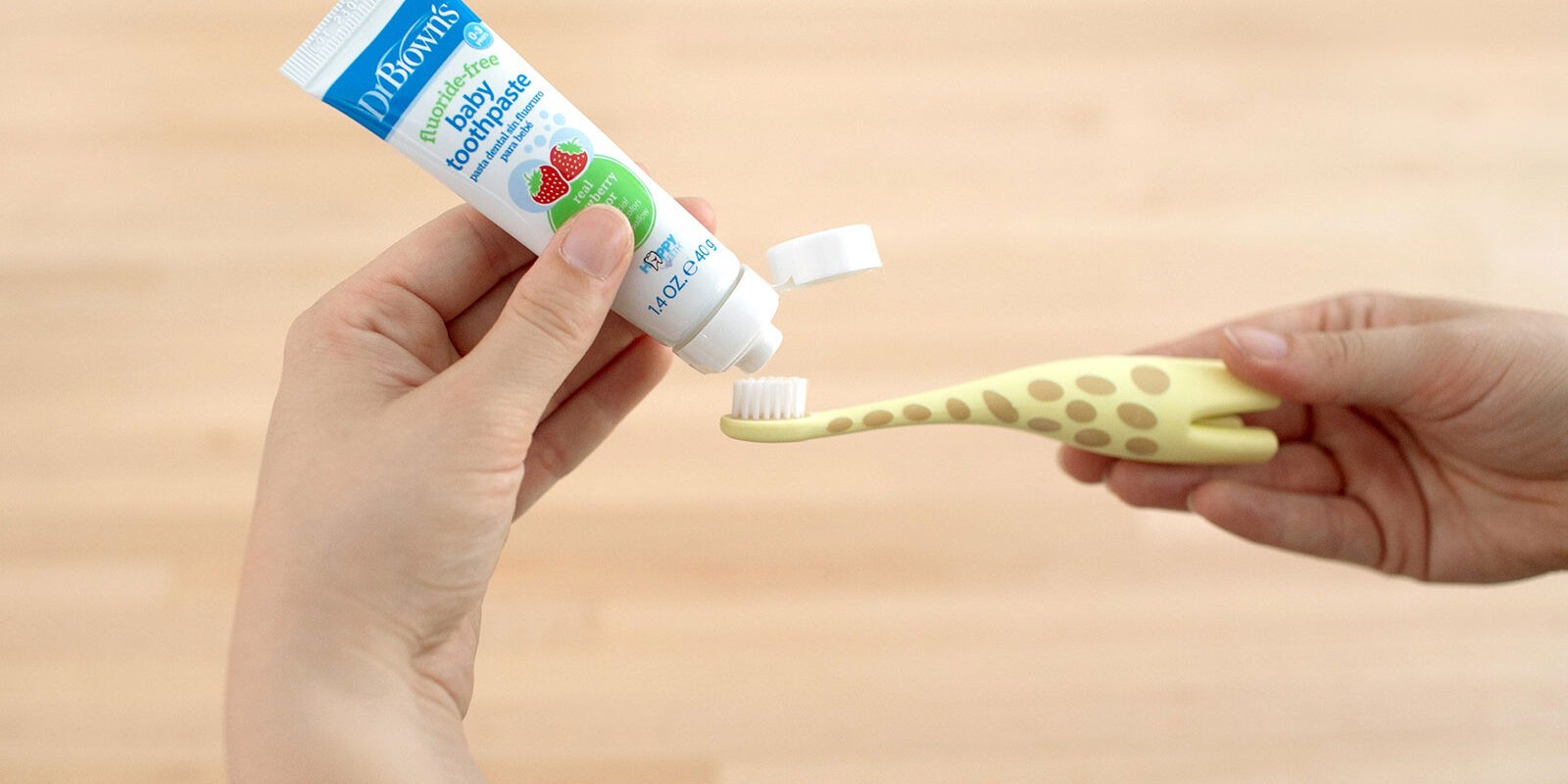 Hands putting toothpaste onto giraffe toothbrush