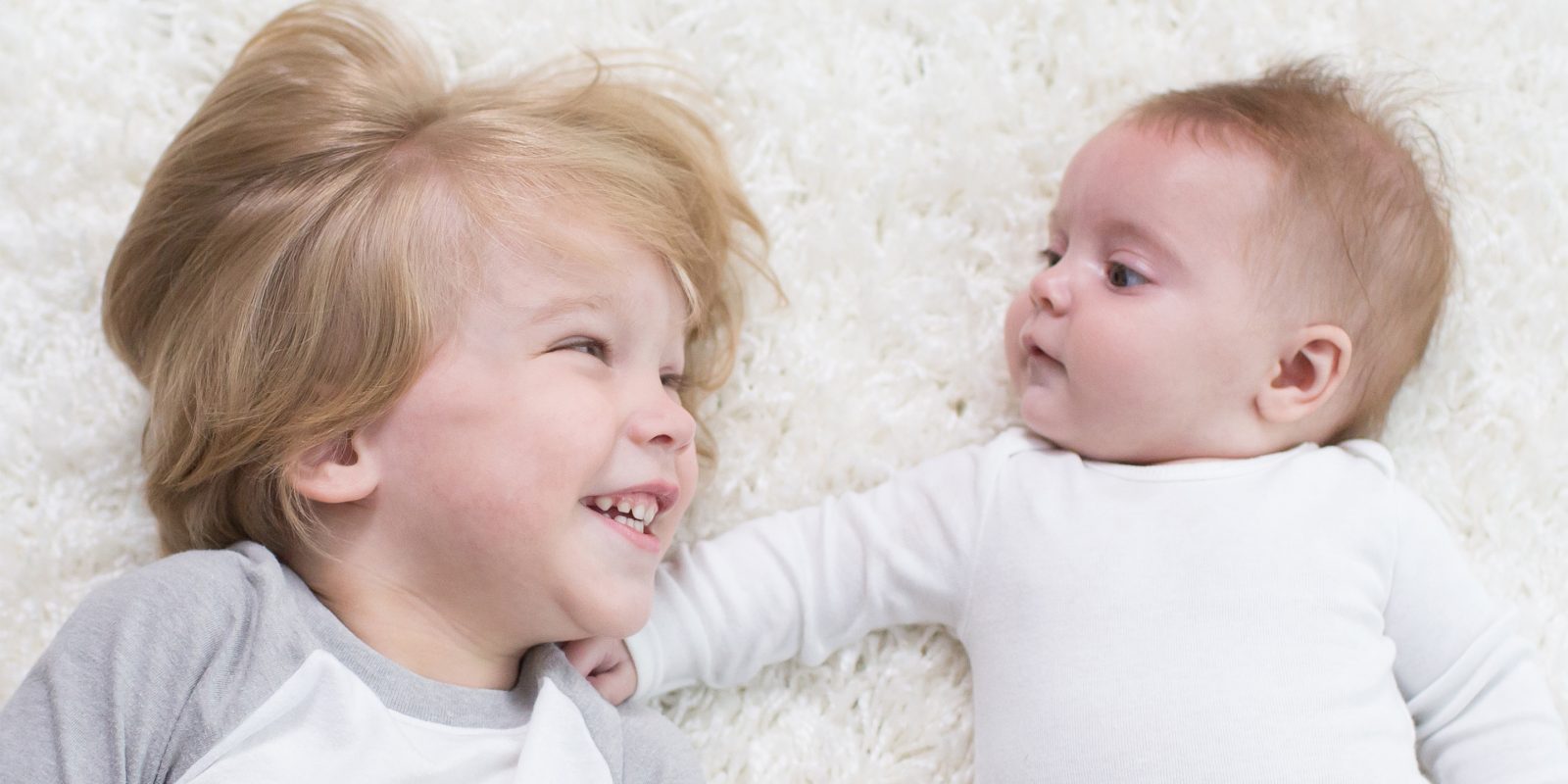 Toddler and baby laying on rug together