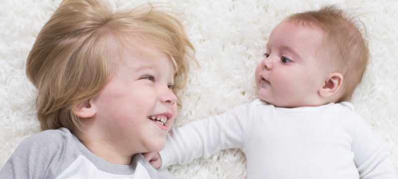 Toddler and baby laying on rug together