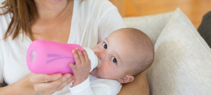 Baby in mother's arms being fed a bottle with a bottle sleeve on it