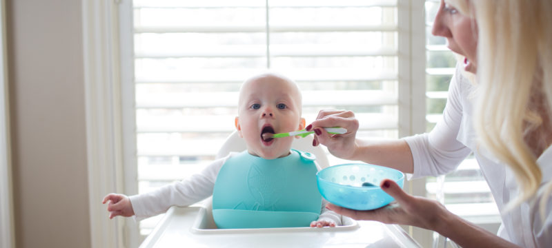 Baby in highchair being fed by mother