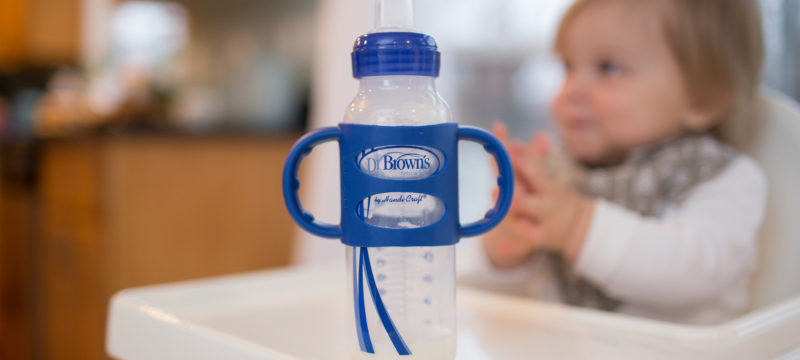 Sippy bottle with silicone handles sitting on highchair table with baby in background