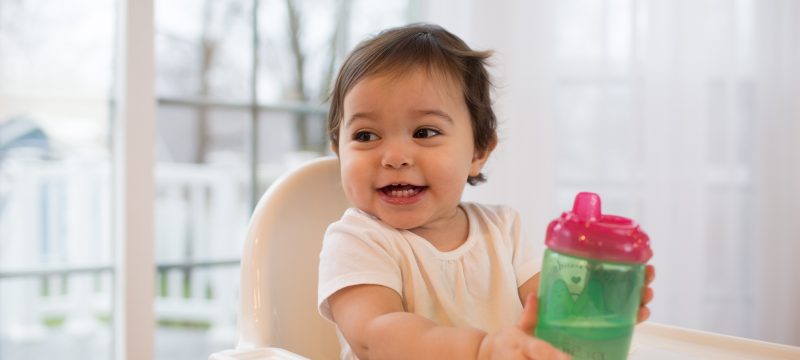 Baby in highchair with cup on table