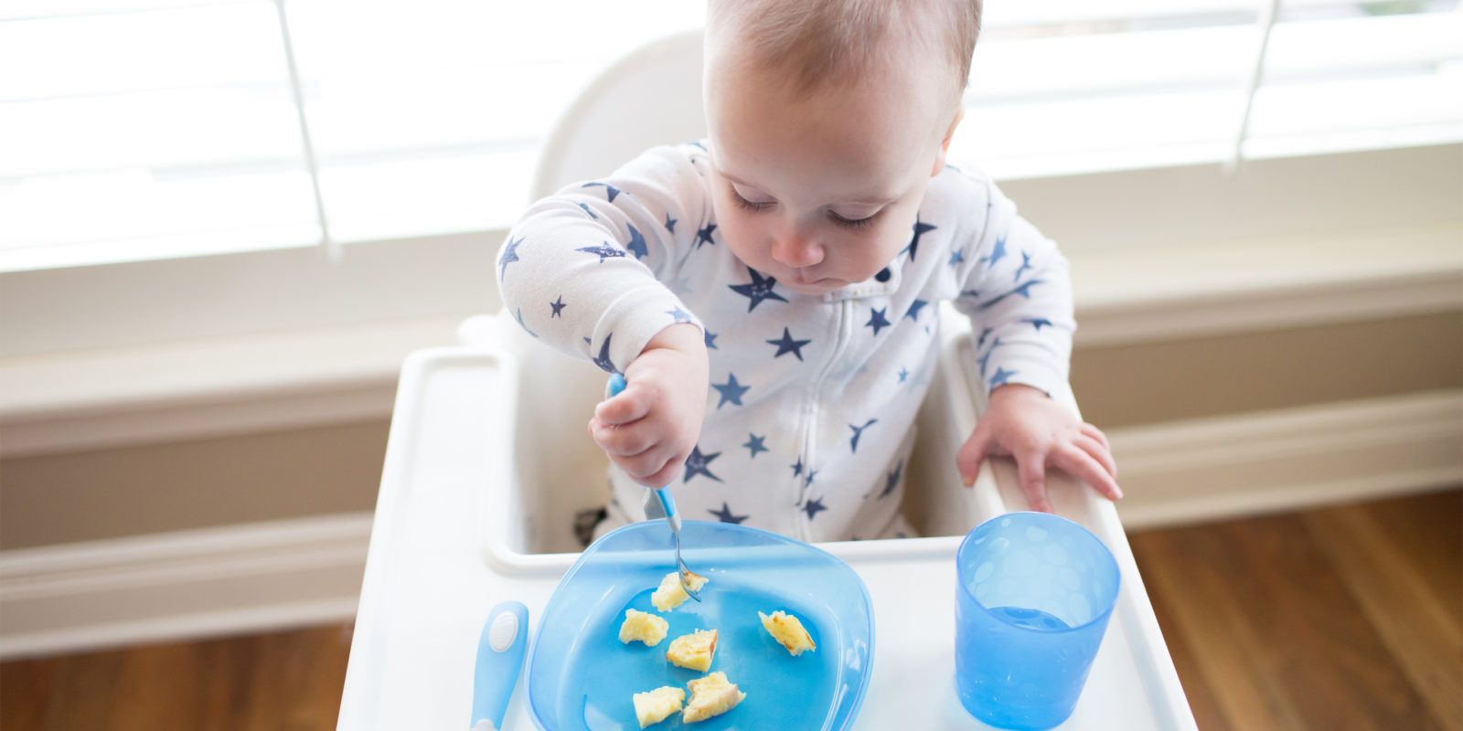 Baby in highchair using form to eat bananas from plate