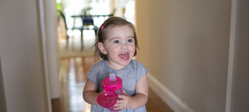 Baby standing in hallway holding sippy cup and laughing