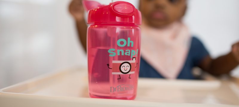 Straw sippy cup on highchair table with baby in background