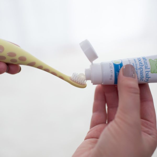 Close up image of a hand putting toothpaste on a giraffe baby toothbrush