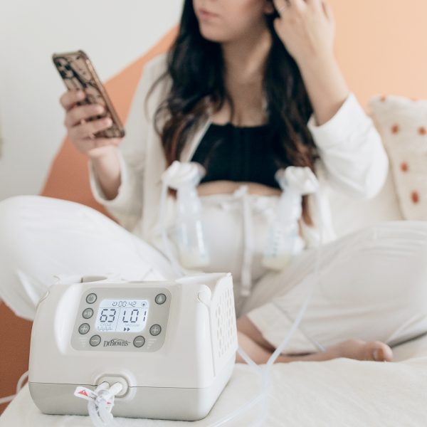 Dr. Brown's Customflow Double Electric Breast Pump being used by a mom seated using her smartphone while pumping hands-free