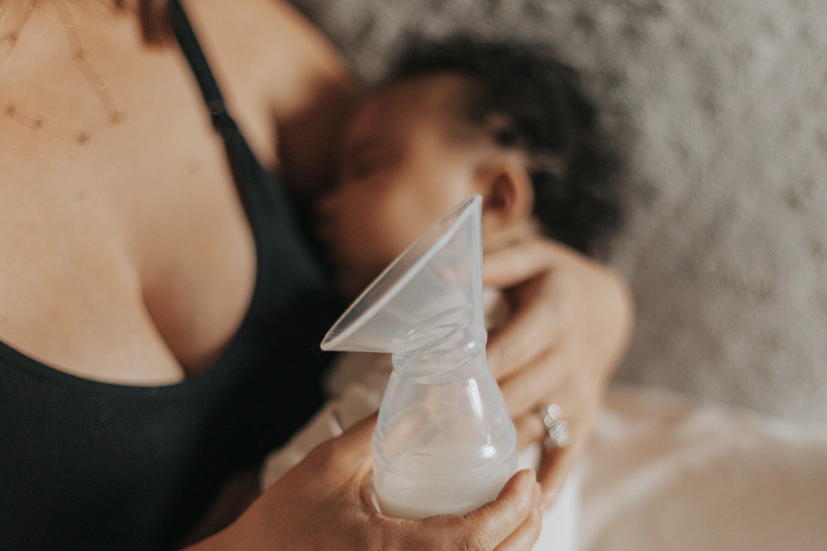 Breastfeeding mom holding Dr. Brown's Silicone One-Piece Breast Pump while holding baby
