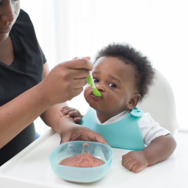 Baby in high chair being spoon fed by mom from scoop a bowl