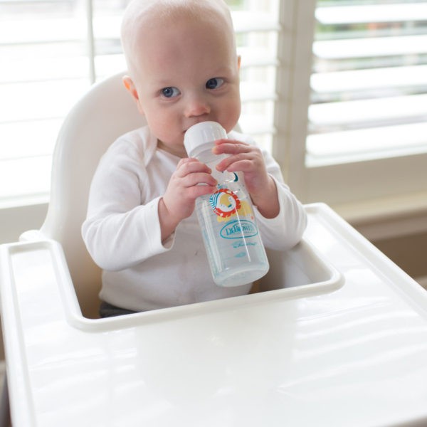Baby in high chair drinking from lion sippy bottle