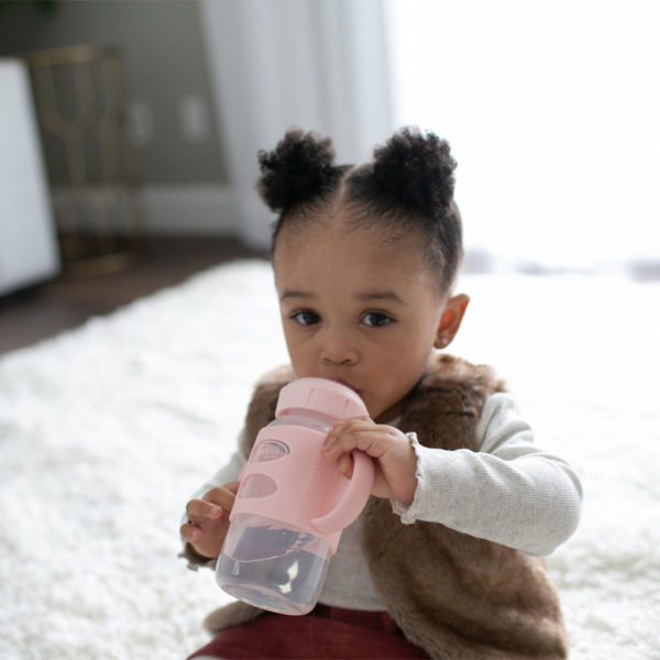 Toddler holding a Light Pink Milestones™ Wide-Neck Sippy Bottle with Silicone Handles