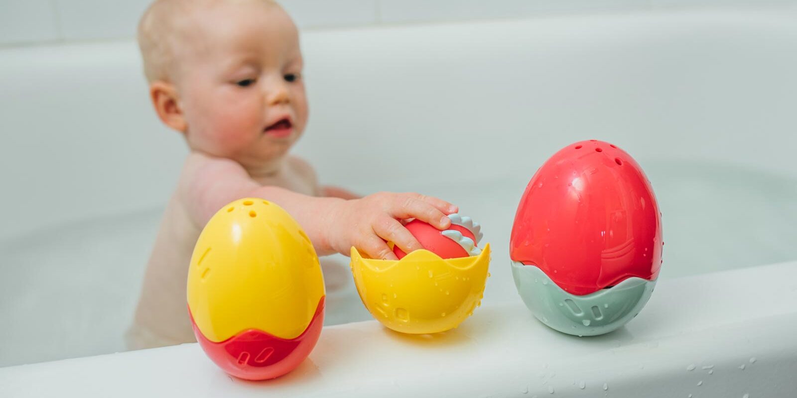 Infant playing with Float and Hatch Dino Egg bath toys