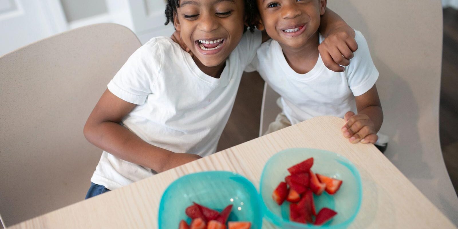 Two toddlers in front of bowls of strawberries