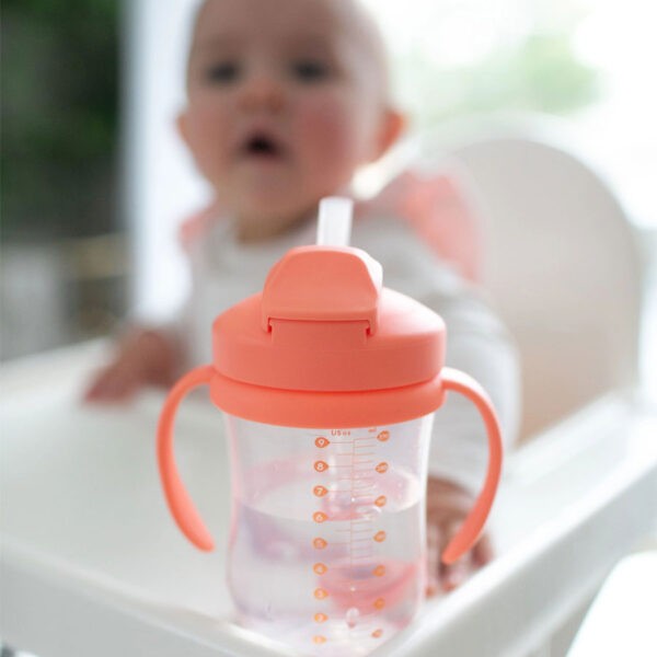 Coral straw cup with infant sitting in background