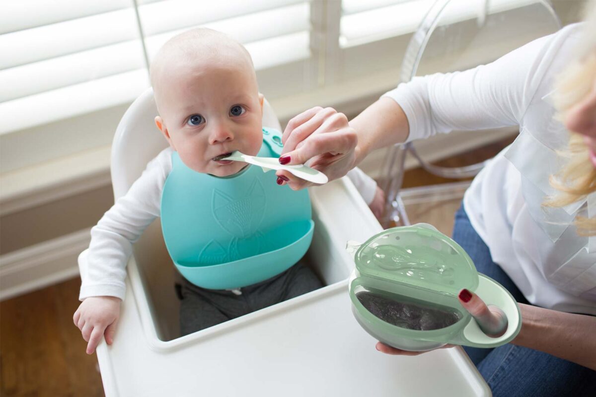 Infant being fed with bowl and light green spoon
