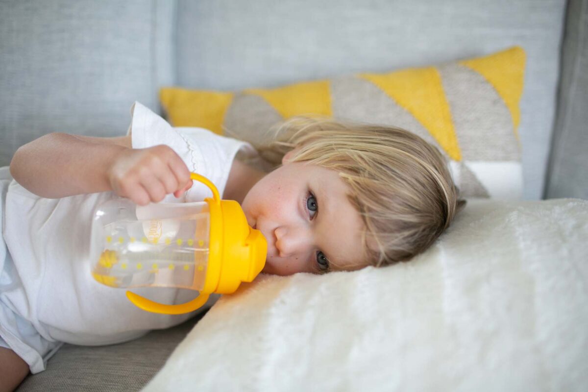 Toddler lying down holding a yellow straw cup