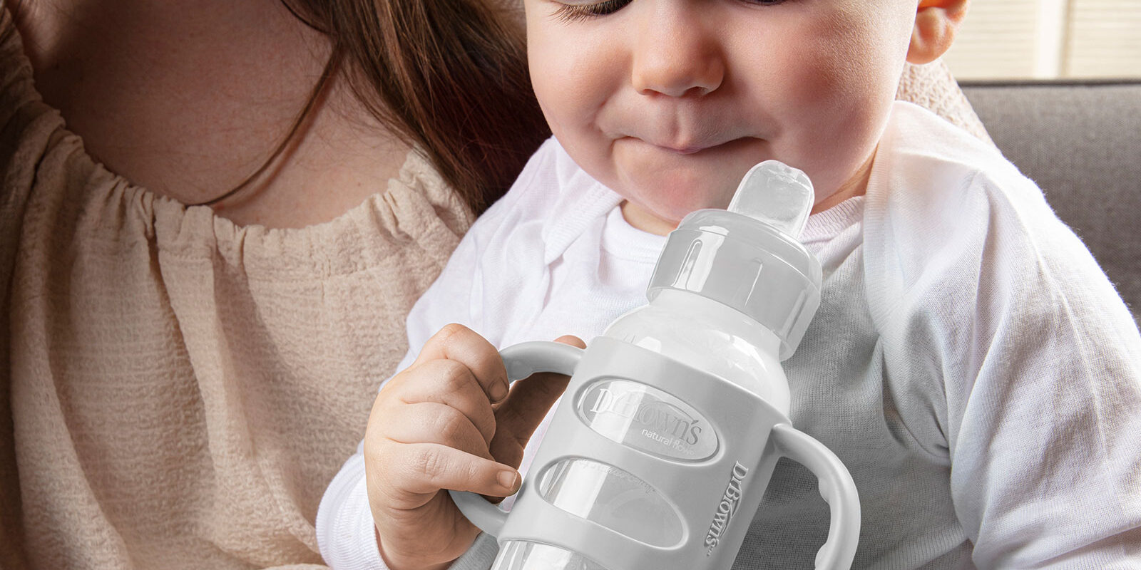 Baby holding a Dr. Brown's Sippy Bottle with silicone handles whiel sitting on his mom's lap