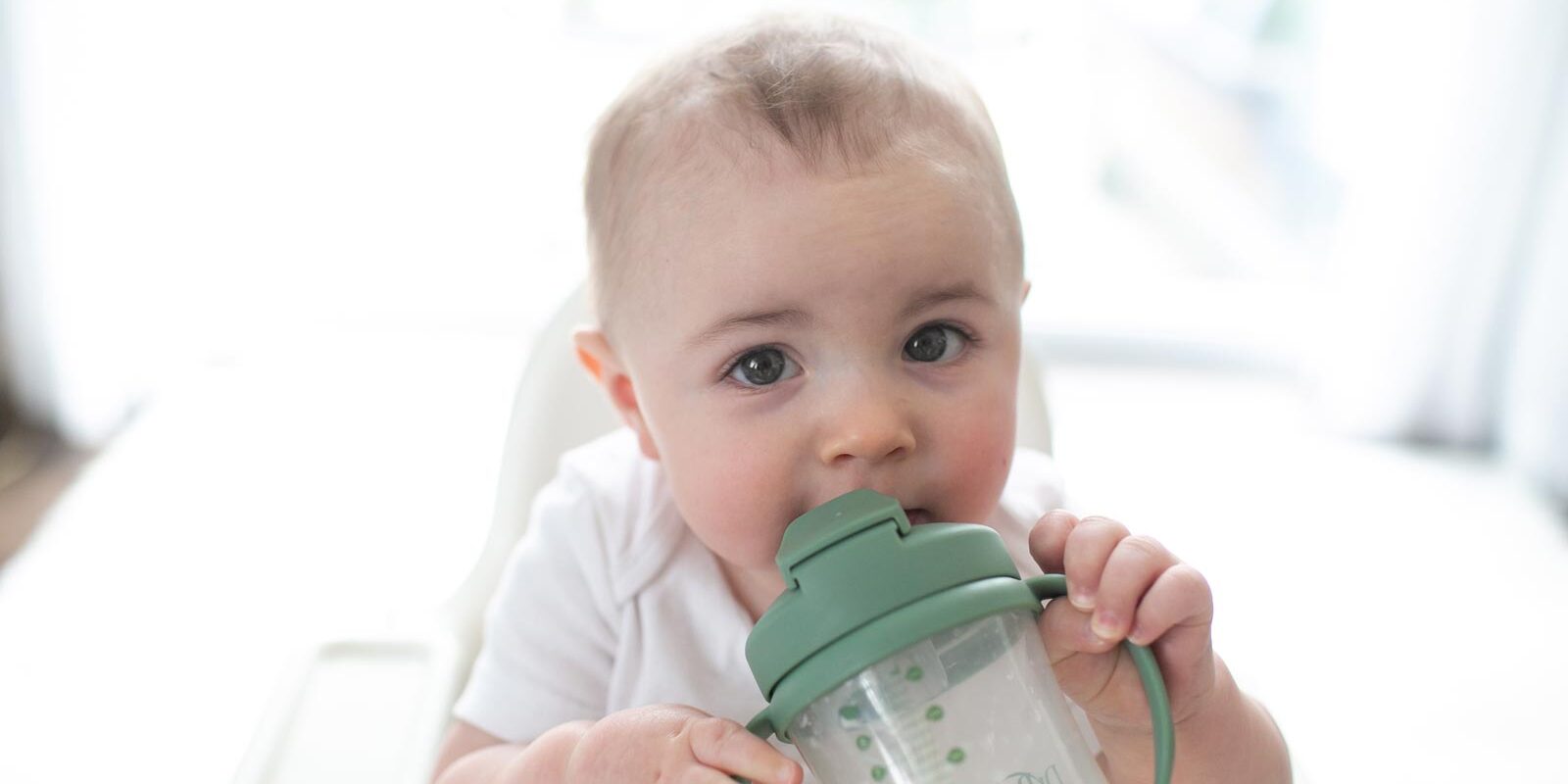 Infant holding and sucking on a straw cup