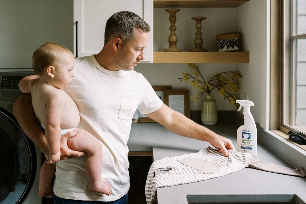 Person holding infant cleaning clothes with laundry spray